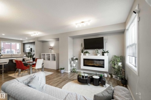 Living area featuring wood finished floors, a glass covered fireplace, and a textured ceiling - 31 2803 James Mowatt Trail, Edmonton, AB - Indoor Photo Showing Living Room With Fireplace