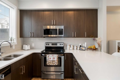 Kitchen with appliances with stainless steel finishes, dark brown cabinetry, and modern cabinets - 31 2803 James Mowatt Trail, Edmonton, AB - Indoor Photo Showing Kitchen With Double Sink With Upgraded Kitchen