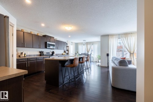 Kitchen with a center island with sink, dark wood finish cabinets, a breakfast bar area, stainless steel appliances, and a textured ceiling - 3312 17B Avenue, Edmonton, AB - Indoor Photo Showing Kitchen