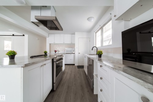 Kitchen featuring a barn door, range hood, stainless steel appliances, white cabinetry, and dark wood finished floors - 11430 81 Street, Edmonton, AB - Indoor Photo Showing Kitchen With Upgraded Kitchen