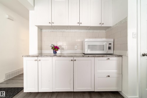 Kitchen view of white cabinets, white microwave, wood finished floors, and tasteful backsplash - 11430 81 Street, Edmonton, AB - Indoor Photo Showing Kitchen
