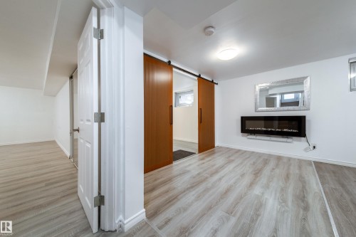 Unfurnished living room featuring a barn door, light wood-type flooring, and a glass covered fireplace - 11430 81 Street, Edmonton, AB - Indoor Photo Showing Other Room With Fireplace