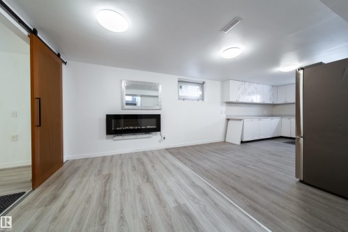 Unfurnished living room with a barn door, light wood-type flooring, and a glass covered fireplace - 11430 81 Street, Edmonton, AB - Indoor Photo Showing Other Room With Fireplace