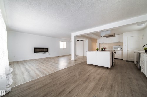 Unfurnished living room with light wood-style floors, a textured ceiling, and a glass covered fireplace - 11430 81 Street, Edmonton, AB - Indoor