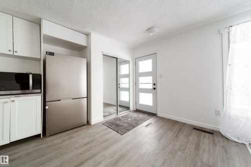 Kitchen featuring stainless steel appliances, white cabinets, a textured ceiling, and light wood-type flooring - 11430 81 Street, Edmonton, AB - Indoor Photo Showing Other Room