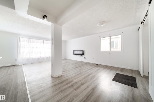 Unfurnished living room with light wood-style floors, a textured ceiling, and heating unit - 11430 81 Street, Edmonton, AB - Indoor Photo Showing Other Room