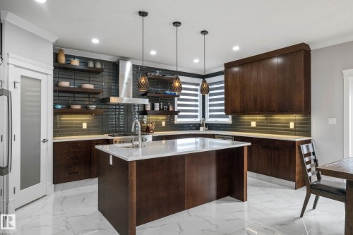 Kitchen with a center island with sink, dark wood finish cabinets, decorative light fixtures, light stone counters, and open shelves - 4086 Whispering River Drive, Edmonton, AB - Indoor Photo Showing Kitchen With Upgraded Kitchen
