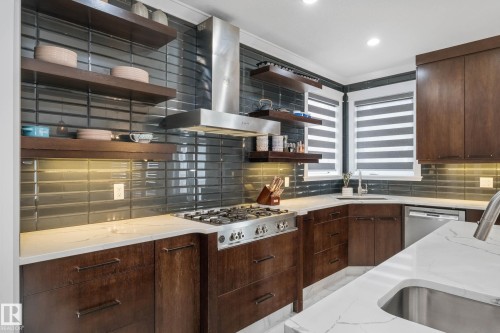 Kitchen featuring dark wood finish cabinets, backsplash, stainless steel appliances, and light stone countertops - 4086 Whispering River Drive, Edmonton, AB - Indoor Photo Showing Kitchen With Upgraded Kitchen