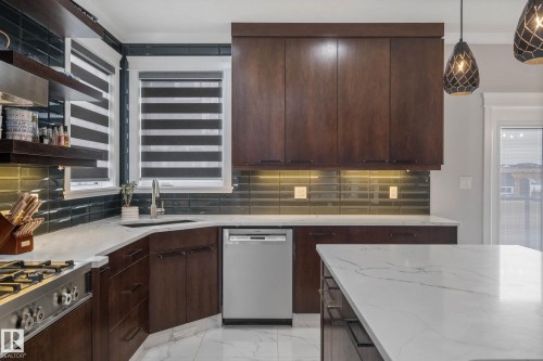 Kitchen with dark wood finish cabinets, stainless steel appliances, light marble finish floors, light stone countertops, and tasteful backsplash - 4086 Whispering River Drive, Edmonton, AB - Indoor Photo Showing Kitchen