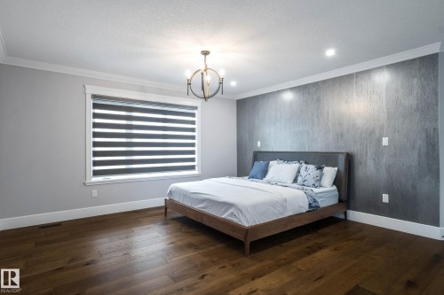 Bedroom with an accent wall, dark wood-style floors, ornamental molding, and suspended lighting - 4086 Whispering River Drive, Edmonton, AB - Indoor Photo Showing Bedroom