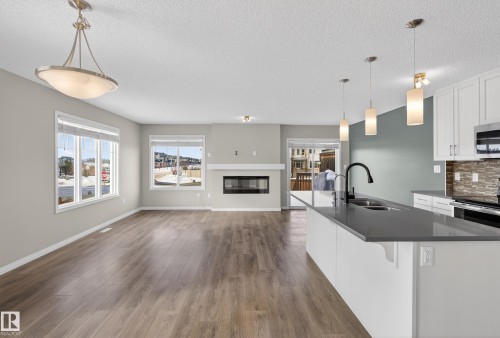 Kitchen with white cabinetry, hanging light fixtures, dark wood-style flooring, open floor plan, and stainless steel appliances - 2704 Coughlan Green, Edmonton, AB - Indoor Photo Showing Kitchen With Double Sink With Upgraded Kitchen