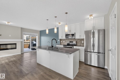 Kitchen featuring stainless steel appliances, white cabinets, dark wood-style floors, a breakfast bar, and a textured ceiling - 2704 Coughlan Green, Edmonton, AB - Indoor Photo Showing Kitchen With Fireplace With Upgraded Kitchen