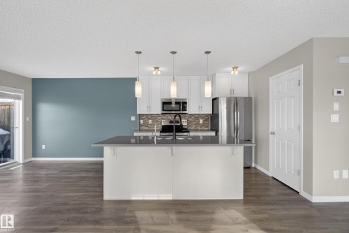 Kitchen featuring a center island with sink, a breakfast bar area, white cabinetry, stainless steel appliances, and dark wood-style floors - 2704 Coughlan Green, Edmonton, AB - Indoor Photo Showing Kitchen With Upgraded Kitchen