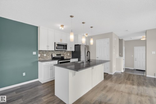Kitchen with white cabinetry, stainless steel appliances, dark wood-type flooring, a kitchen bar, and a textured ceiling - 2704 Coughlan Green, Edmonton, AB - Indoor Photo Showing Kitchen With Upgraded Kitchen