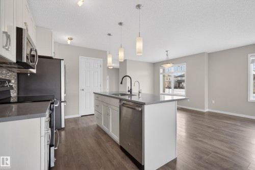 Kitchen featuring stainless steel appliances, white cabinetry, hanging light fixtures, a kitchen island with sink, and a textured ceiling - 2704 Coughlan Green, Edmonton, AB - Indoor Photo Showing Kitchen With Upgraded Kitchen