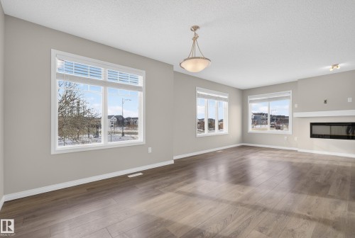 Unfurnished living room with dark wood-style flooring, a glass covered fireplace, and a textured ceiling - 2704 Coughlan Green, Edmonton, AB - Indoor With Fireplace