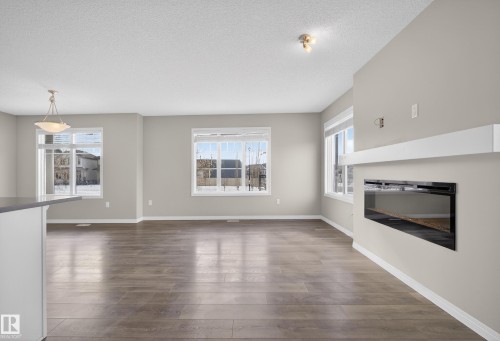 Unfurnished living room featuring dark wood-style flooring, a glass covered fireplace, and a textured ceiling - 2704 Coughlan Green, Edmonton, AB - Indoor Photo Showing Living Room With Fireplace