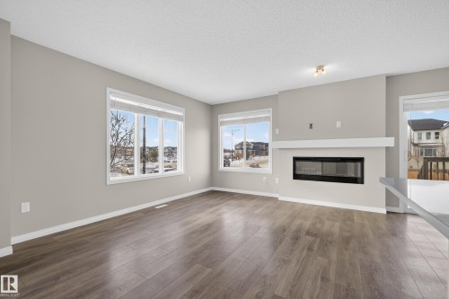 Unfurnished living room featuring a glass covered fireplace, dark wood finished floors, and a textured ceiling - 2704 Coughlan Green, Edmonton, AB - Indoor Photo Showing Living Room With Fireplace