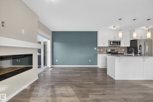Kitchen with a kitchen bar, stainless steel appliances, white cabinets, dark wood-type flooring, and tasteful backsplash - 2704 Coughlan Green, Edmonton, AB - Indoor Photo Showing Kitchen With Fireplace With Upgraded Kitchen