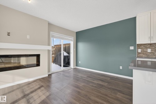 Unfurnished living room featuring a glass covered fireplace, dark wood-style floors, and a textured ceiling - 2704 Coughlan Green, Edmonton, AB - Indoor Photo Showing Living Room With Fireplace