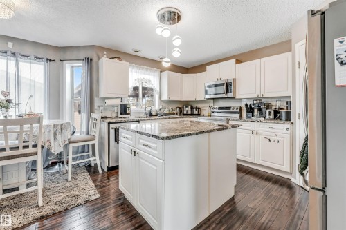 Kitchen featuring stainless steel appliances, light stone counters, white cabinets, dark wood-style flooring, and a textured ceiling - 4404 150 Avenue, Edmonton, AB - Indoor Photo Showing Kitchen With Upgraded Kitchen