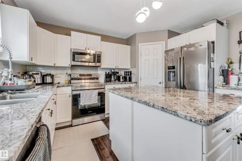 Kitchen with stainless steel appliances, a kitchen island, light stone countertops, dark wood-style flooring, and a textured ceiling - 4404 150 Avenue, Edmonton, AB - Indoor Photo Showing Kitchen With Upgraded Kitchen
