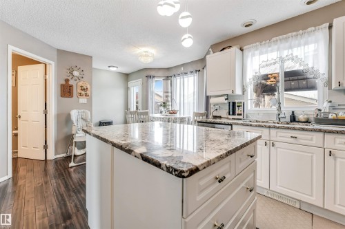 Kitchen with white cabinetry, a kitchen island, light stone countertops, a textured ceiling, and hanging light fixtures - 4404 150 Avenue, Edmonton, AB - Indoor Photo Showing Kitchen With Upgraded Kitchen