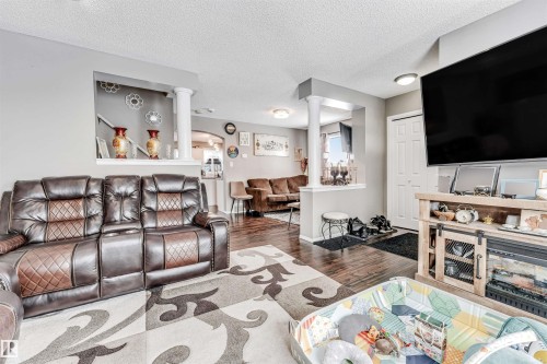 Living area featuring decorative columns, dark wood finished floors, a textured ceiling, and arched walkways - 4404 150 Avenue, Edmonton, AB - Indoor Photo Showing Living Room
