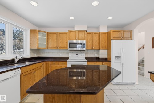 Kitchen with white appliances, decorative backsplash, dark stone countertops, light tile patterned flooring, and recessed lighting - 11435 37A Avenue, Edmonton, AB - Indoor Photo Showing Kitchen With Double Sink