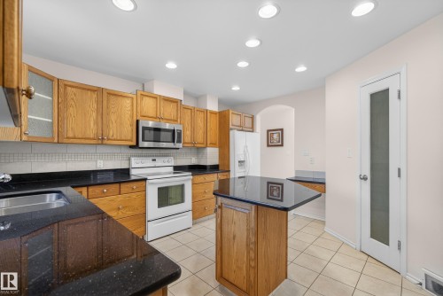 Kitchen with glass insert cabinets, a center island, white appliances, arched walkways, and wood finish cabinetry - 11435 37A Avenue, Edmonton, AB - Indoor Photo Showing Kitchen With Double Sink