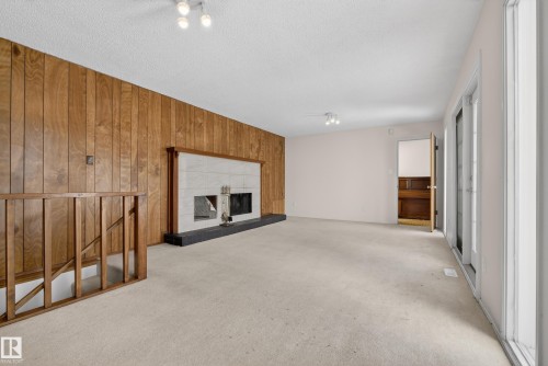 Unfurnished living room featuring wooden walls, a fireplace with raised hearth, and light carpet - 11435 37A Avenue, Edmonton, AB - Indoor With Fireplace