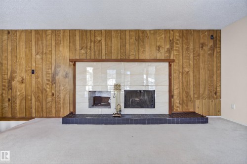 Detailed view of a tiled fireplace, a textured ceiling, carpet, and wooden walls - 11435 37A Avenue, Edmonton, AB - Indoor Photo Showing Other Room With Fireplace