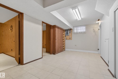 Below grade area with a textured ceiling, wooden walls, light floors, and electric panel - 11435 37A Avenue, Edmonton, AB - Indoor