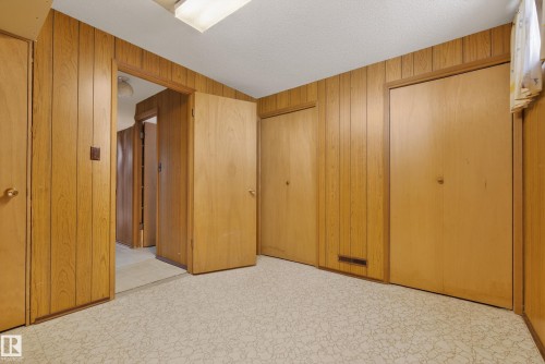 Unfurnished bedroom with multiple closets, wooden walls, a textured ceiling, and light floors - 11435 37A Avenue, Edmonton, AB - Indoor Photo Showing Other Room