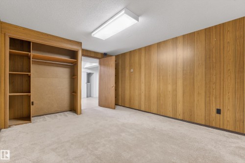 Unfurnished bedroom with light carpet, a closet, wooden walls, and a textured ceiling - 11435 37A Avenue, Edmonton, AB - Indoor Photo Showing Other Room
