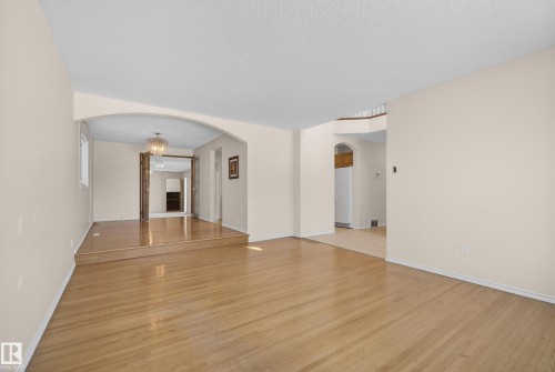 Unfurnished living room featuring arched walkways, light wood-style flooring, a textured ceiling, and hanging lights - 11435 37A Avenue, Edmonton, AB - Indoor Photo Showing Other Room