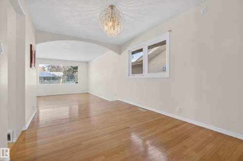Empty room with arched walkways, a textured ceiling, light wood-type flooring, and a chandelier - 11435 37A Avenue, Edmonton, AB - Indoor Photo Showing Other Room