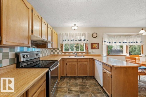 Kitchen with stainless steel electric stove, a peninsula, light countertops, under cabinet range hood, and backsplash - 10429 28A Avenue, Edmonton, AB - Indoor Photo Showing Kitchen With Double Sink