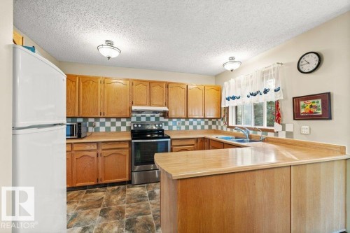 Kitchen with appliances with stainless steel finishes, backsplash, light countertops, a peninsula, and a textured ceiling - 10429 28A Avenue, Edmonton, AB - Indoor Photo Showing Kitchen With Double Sink