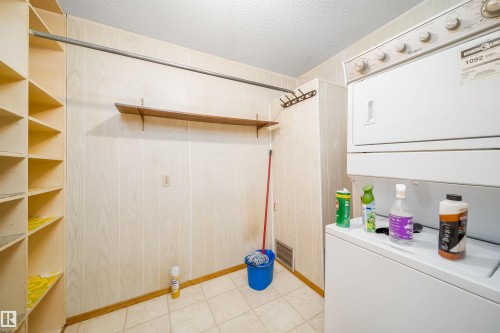 Laundry area featuring a textured ceiling, stacked washer and dryer, and wooden walls - 8908 130 Avenue Nw, Edmonton, AB - Indoor