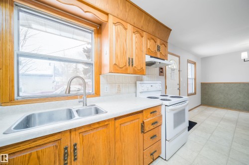 Kitchen with white electric stove, light countertops, light flooring, wood finish cabinets, and a wainscoted wall - 8908 130 Avenue Nw, Edmonton, AB - Indoor Photo Showing Kitchen With Double Sink