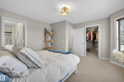 Bedroom with a spacious closet, light colored carpet, a textured ceiling, and ensuite bath - 44 903 Rutherford Road, Edmonton, AB - Indoor Photo Showing Bedroom
