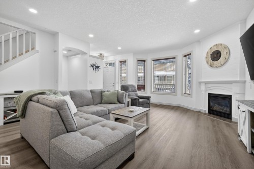 Living room featuring a textured ceiling, wood finished floors, a glass covered fireplace, recessed lighting, and arched walkways - 44 903 Rutherford Road, Edmonton, AB - Indoor Photo Showing Living Room With Fireplace