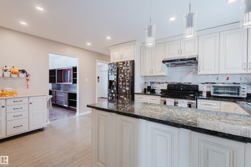 Kitchen featuring dark stone counters, stainless steel appliances, backsplash, light wood-style floors, and white cabinetry - 11519 37A Avenue, Edmonton, AB - Indoor Photo Showing Kitchen With Upgraded Kitchen