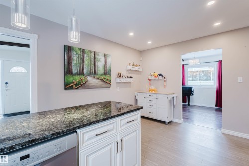 Kitchen with dishwasher, dark stone countertops, white cabinets, and hanging light fixtures - 11519 37A Avenue, Edmonton, AB - Indoor Photo Showing Kitchen