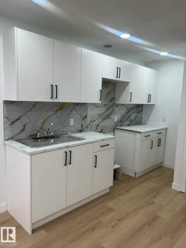 This kitchen features white cabinetry with black hardware, a tiled backsplash with a marble pattern, and light wood-style flooring - 9194 Pear Drive Sw, Edmonton, AB - Indoor Photo Showing Kitchen
