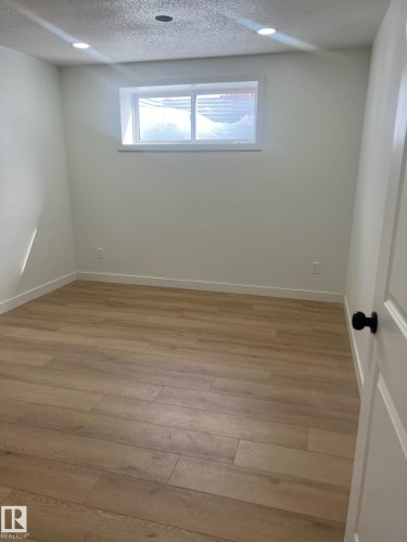 This room features light wood-look flooring, recessed ceiling lights, and a window providing natural light - 9194 Pear Drive Sw, Edmonton, AB - Indoor Photo Showing Other Room