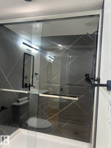 The bathroom features a spacious shower with glass enclosure, black framed mirror, and modern lighting fixtures - 9194 Pear Drive Sw, Edmonton, AB - Indoor