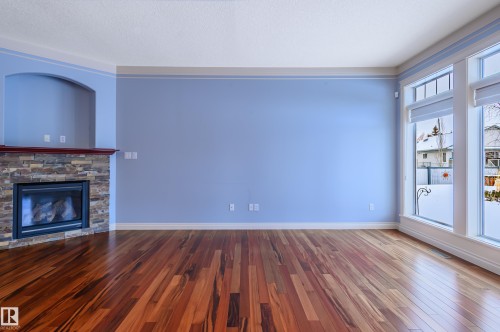 Unfurnished living room with hardwood / wood-style floors, a stone fireplace, and a textured ceiling - 48 Fairway Point(E), Spruce Grove, AB - Indoor Photo Showing Living Room With Fireplace