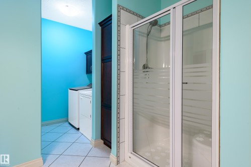 Bathroom featuring a stall shower, washer and clothes dryer, light tile patterned flooring, and vanity - 48 Fairway Point(E), Spruce Grove, AB - Indoor Photo Showing Bathroom